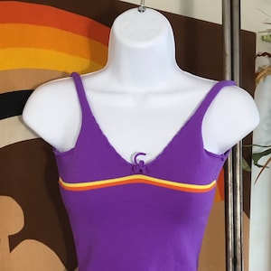 Pode incluir: Top roxo de malha canelada com uma faixa amarela e laranja no peito. O top tem um pequeno la&ccedil;o na gola.