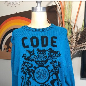 May include: A blue knitted sweater with a black design featuring the word "CODE" and a stylized graphic.