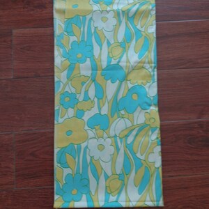 May include: A white fabric with a repeating pattern of blue, yellow, and white flowers. The fabric has a retro 1960s or 1970s style.