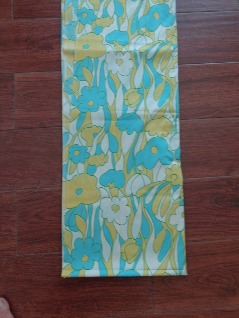 May include: A white fabric with a repeating pattern of blue, yellow, and white flowers. The fabric has a retro 1960s or 1970s style.
