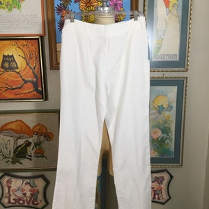 May include: White wide-leg pants with a straight leg and a center crease. The pants are hanging on a white mannequin.