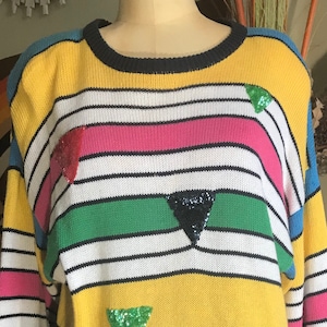 May include: A colorful striped sweater with black, white, yellow, pink, green, and blue stripes. The sweater has sequined triangles in various colors.