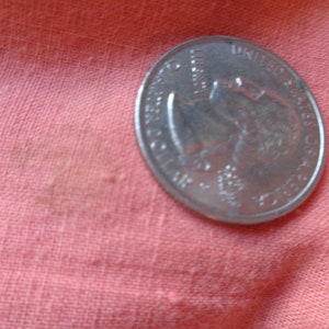 May include: A silver US quarter coin with the profile of George Washington on the obverse side. The coin is lying on a pink fabric surface.
