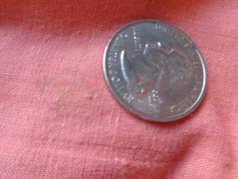 May include: A silver US quarter coin with the profile of George Washington on the obverse side. The coin is lying on a pink fabric surface.