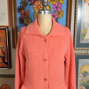 May include: A peach-colored cardigan with a button-up front and long sleeves. The cardigan is made of a soft, fuzzy material.