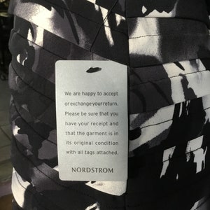 May include: A white tag with black text attached to a black and white patterned dress. The tag reads: "We are happy to accept or exchange your return. Please be sure that you have your receipt and that the garment is in its original condition with all tags attached. NORDSTROM"