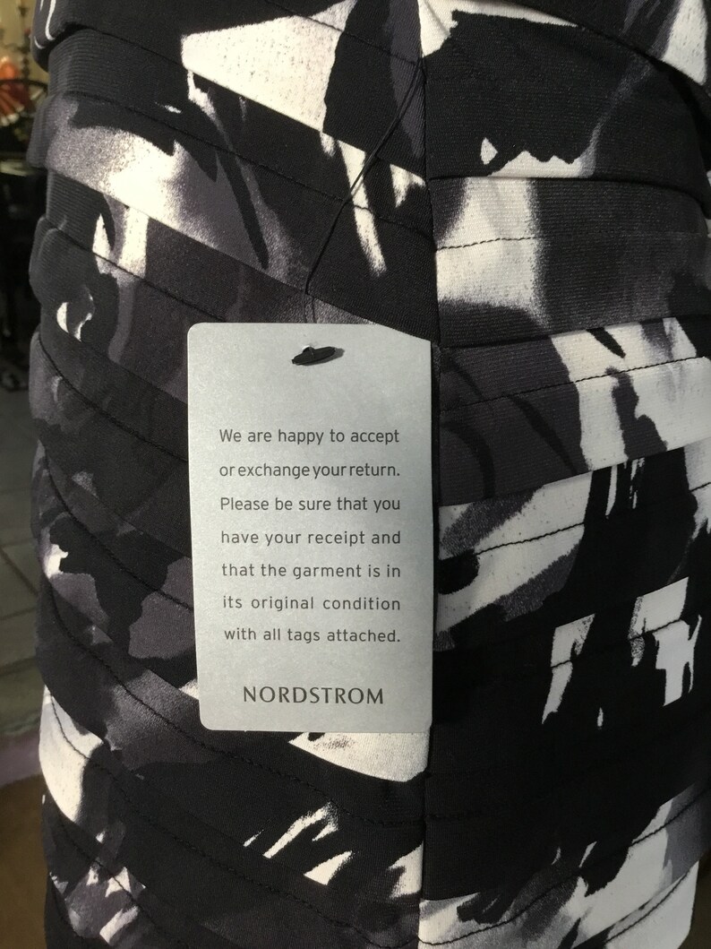 May include: A white tag with black text attached to a black and white patterned dress. The tag reads: "We are happy to accept or exchange your return. Please be sure that you have your receipt and that the garment is in its original condition with all tags attached. NORDSTROM"