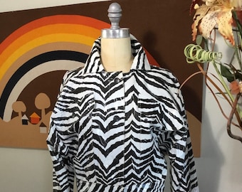 May include: A white and black zebra print jacket with a button closure. The jacket has long sleeves and two pockets on the front.