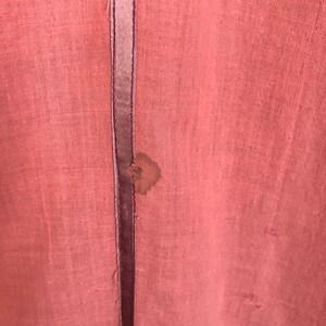 May include: A close-up of a pink fabric with a dark brown seam down the center. There is a small brown stain on the fabric.