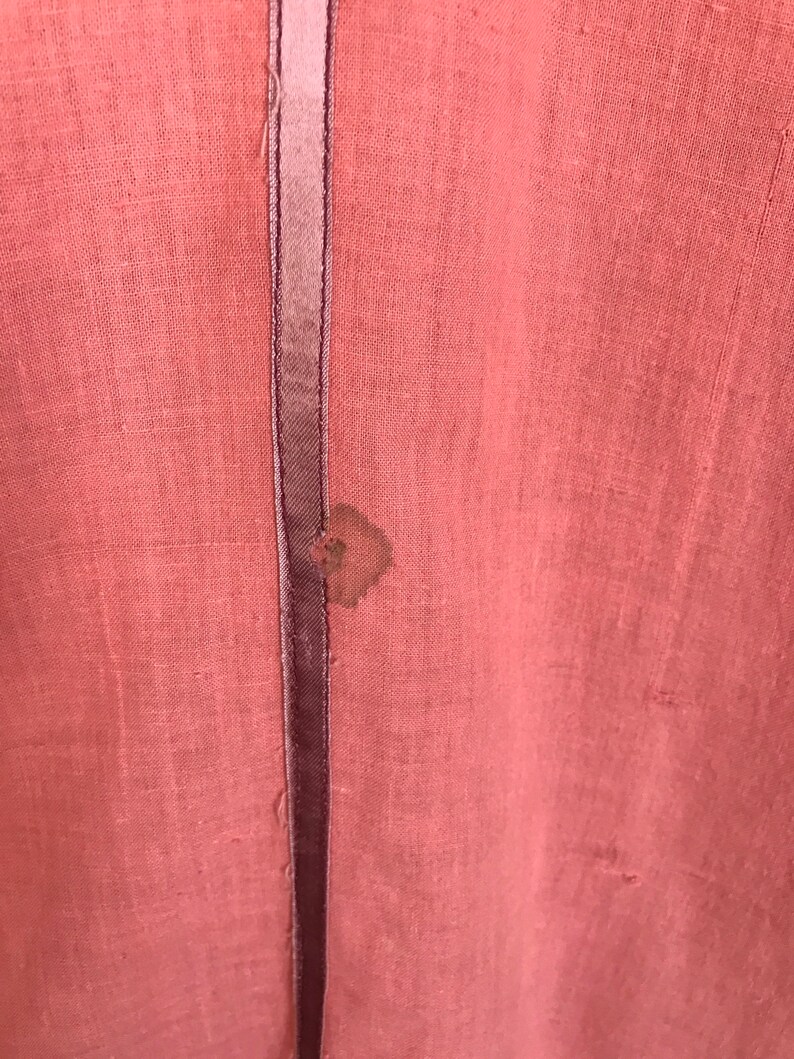 May include: A close-up of a pink fabric with a dark brown seam down the center. There is a small brown stain on the fabric.