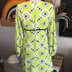 May include: A lime green mini dress with a white and navy blue geometric pattern. The dress has long sleeves and a back zipper.