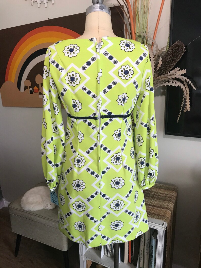 May include: A lime green mini dress with a white and navy blue geometric pattern. The dress has long sleeves and a back zipper.
