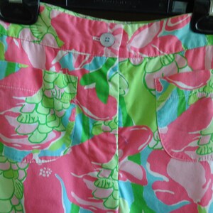 May include: Pink and green patterned shorts with two front pockets. The shorts have a button closure and a floral design.