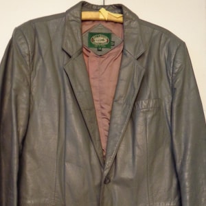 May include: A gray leather blazer with a single button closure and a label that reads "Carriage House" with a logo of a horse and carriage.