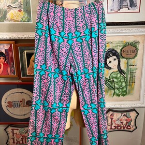 K&ouml;nnte beinhalten: Rosa und t&uuml;rkisfarbene gemusterte Hose mit weitem Bein. Die Hose hat ein geometrisches Muster mit einem sich wiederholenden Design aus stilisierten B&auml;umen.