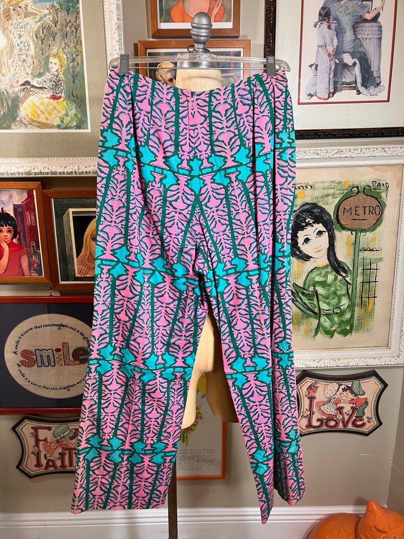 K&ouml;nnte beinhalten: Rosa und t&uuml;rkisfarbene gemusterte Hose mit weitem Bein. Die Hose hat ein geometrisches Muster mit einem sich wiederholenden Design aus stilisierten B&auml;umen.