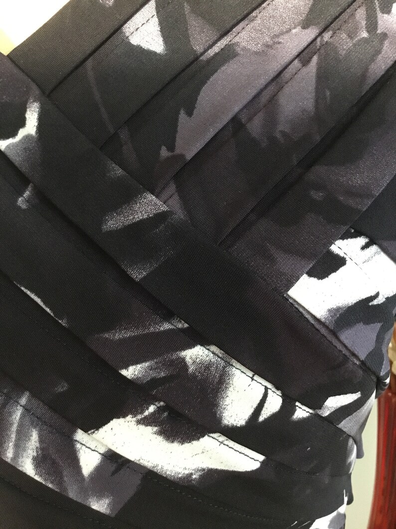 May include: Black and white abstract print fabric with black ribbon accents. The fabric has a soft, flowing texture.