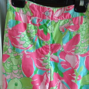 May include: Pink, green, and blue floral print shorts with a button closure. The shorts have two pockets on the front.