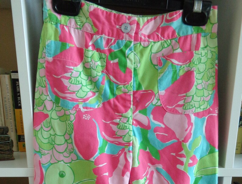 May include: Pink, green, and blue floral print shorts with a button closure. The shorts have two pockets on the front.