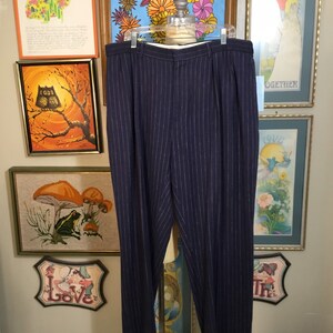 May include: Navy blue pinstripe pants with a white pinstripe. The pants are on a mannequin and are hanging in front of a wall with artwork.