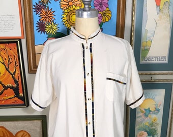 May include: White short-sleeved button-up shirt with a mandarin collar and a colorful trim down the front. The trim features blue, red, yellow, and black stripes.