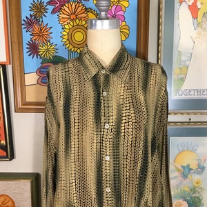 May include: A long-sleeved button-down shirt with a black and gold geometric pattern. The shirt is made of a silky material.