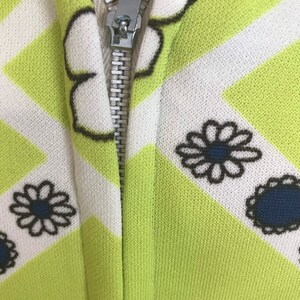 May include: A close-up of a zipper on a green and white patterned fabric. The fabric has a geometric pattern with white lines and black and white flowers.