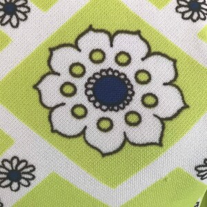 May include: A green fabric with a white and black geometric pattern. The pattern features a large white flower with a blue center and black outline.