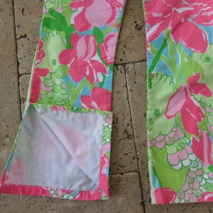 May include: A pair of pink and green pants with a floral print featuring parrots. The pants have a white lining and are made of a soft, lightweight fabric.
