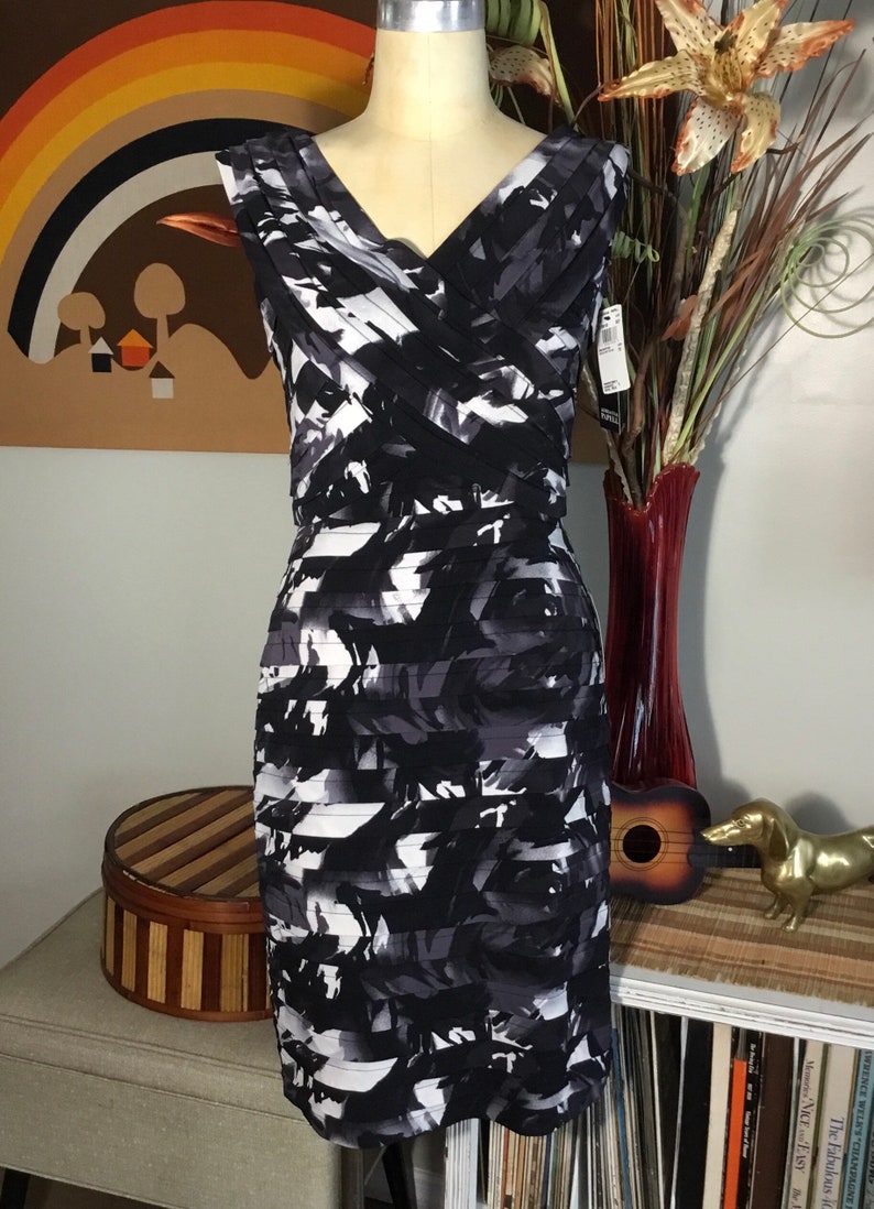 May include: A black and white sleeveless dress with a geometric print. The dress has a v-neckline and a fitted silhouette.