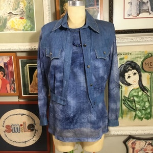May include: A blue denim vest with a tie-dye shirt underneath. The vest has silver studs around the collar and pockets.