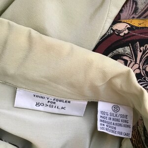 May include: A green silk blouse with a brown, black, and gold patterned design. The tag reads "Timniy-Fowler for 100% Silk" and "100% Silk/Soie Made in Hong Kong Fabrique a Hong Kong RN 63026 See Reverse for Care."