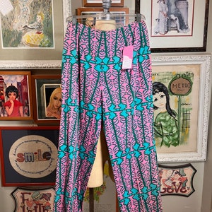 K&ouml;nnte beinhalten: Rosa und t&uuml;rkisfarbene gemusterte Hose mit weitem Bein. Die Hose hat ein geometrisches Muster mit einem sich wiederholenden Design aus t&uuml;rkisfarbenen Bl&auml;ttern und rosa Bl&uuml;ten.