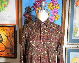May include: A long-sleeved button-down shirt with a paisley print in shades of brown, red, and cream. The shirt has a collared neckline and a button-up front.