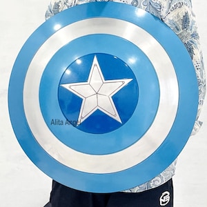 May include: A blue and silver Captain America shield with a white star in the centre. The shield has a circular design with blue, silver, and white concentric rings. The shield is held by a person.