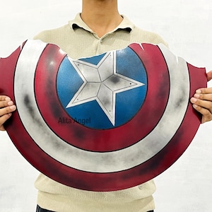 K&ouml;nnte beinhalten: Ein abgenutzter Captain America-Schild mit einem rot-wei&szlig;-blauen Farbschema und einem zentralen Sternemblem. Der Schild hat ein verwittertes Aussehen mit sichtbaren Abnutzungserscheinungen. Es ist eine Requisite oder ein Sammlerst&uuml;ck.