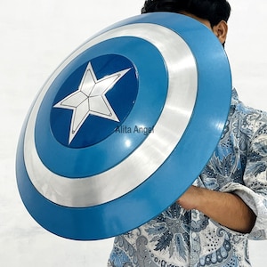 May include: A blue and silver shield with a white star in the centre. The shield has a circular design with a blue outer ring, a silver middle ring, and a blue centre. The shield is held by a person.