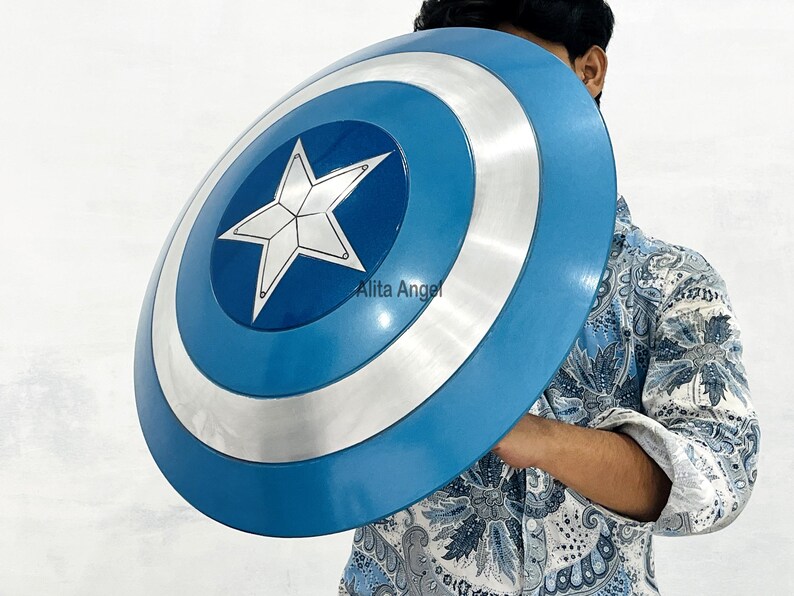 May include: A blue and silver shield with a white star in the centre. The shield has a circular design with a blue outer ring, a silver middle ring, and a blue centre. The shield is held by a person.