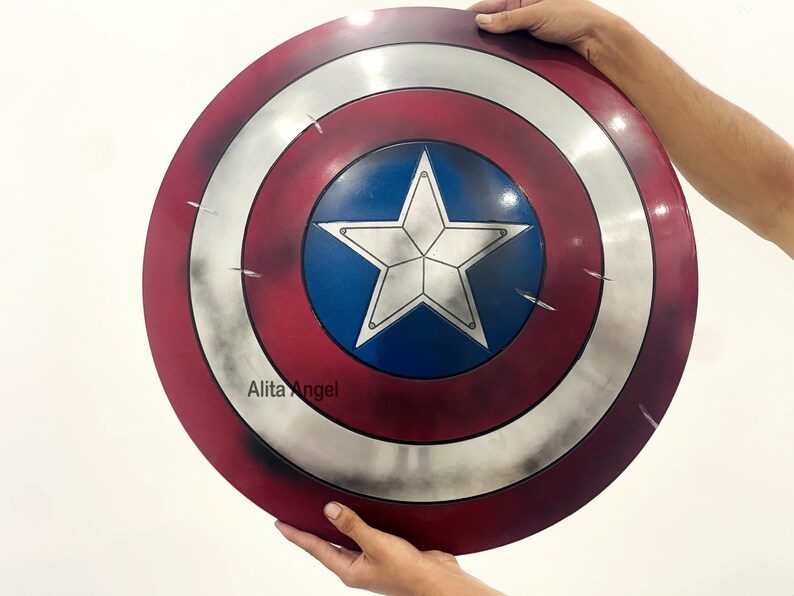 May include: A round shield with a red, white, and blue color scheme. The shield features a white star on a blue center, surrounded by concentric silver and red bands. The shield is held by hands.