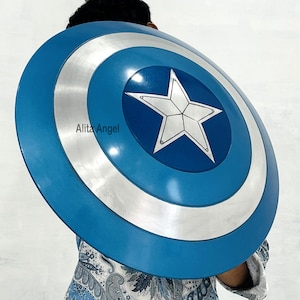 May include: A blue and silver Captain America shield with a white star in the center. The shield has concentric circles of blue and silver. The shield is round and appears to be made of metal. The shield is a prop or costume accessory.