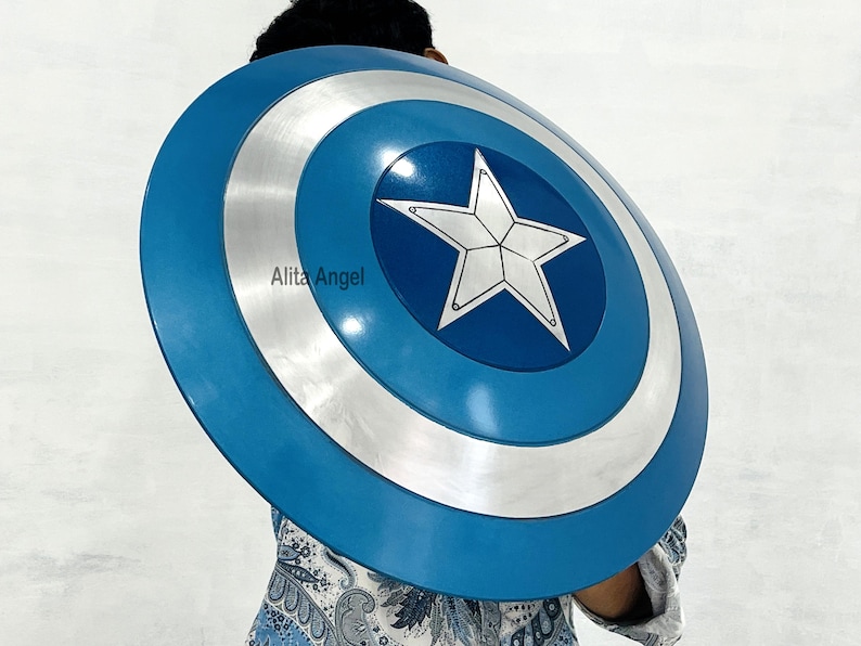 May include: A blue and silver Captain America shield with a white star in the center. The shield has concentric circles of blue and silver. The shield is round and appears to be made of metal. The shield is a prop or costume accessory.
