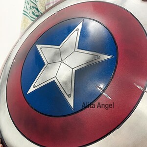 May include: A Captain America shield with a red, white, and blue color scheme. The shield features a white star on a blue center, surrounded by concentric red and silver rings. The shield has a distressed appearance with visible scratches.