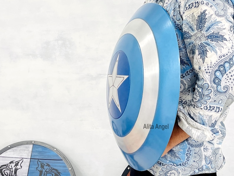 May include: A blue and silver shield with a white star in the centre. The shield has a circular design with a blue outer ring and a silver inner ring. The shield is held by a person.