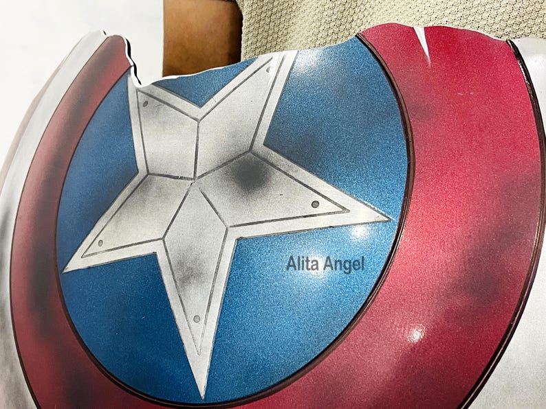 K&ouml;nnte beinhalten: Eine Nachbildung des Captain America-Schildes mit einem zentralen blauen Kreis mit einem wei&szlig;en Stern, umgeben von roten und wei&szlig;en Ringen. Auf dem Schild steht der Text "Alita Angel" auf dem blauen Kreis.