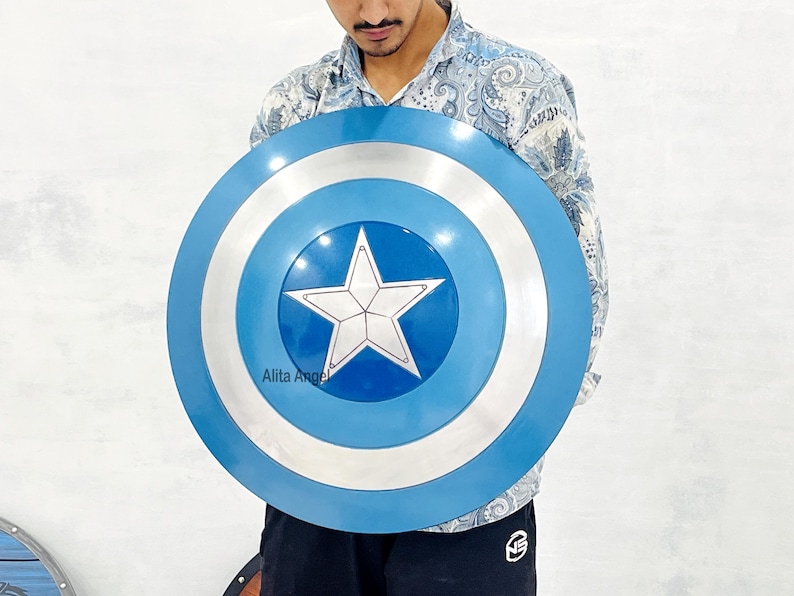 May include: A blue and silver Captain America shield with a white star in the centre. The shield has a circular design with blue, silver, and white concentric rings. The shield is held by a person.