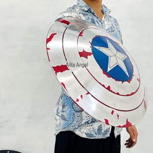 May include: A silver and red Captain America shield with a blue star emblem. The shield has a distressed finish and is round in shape. The shield is a prop or collectible item.
