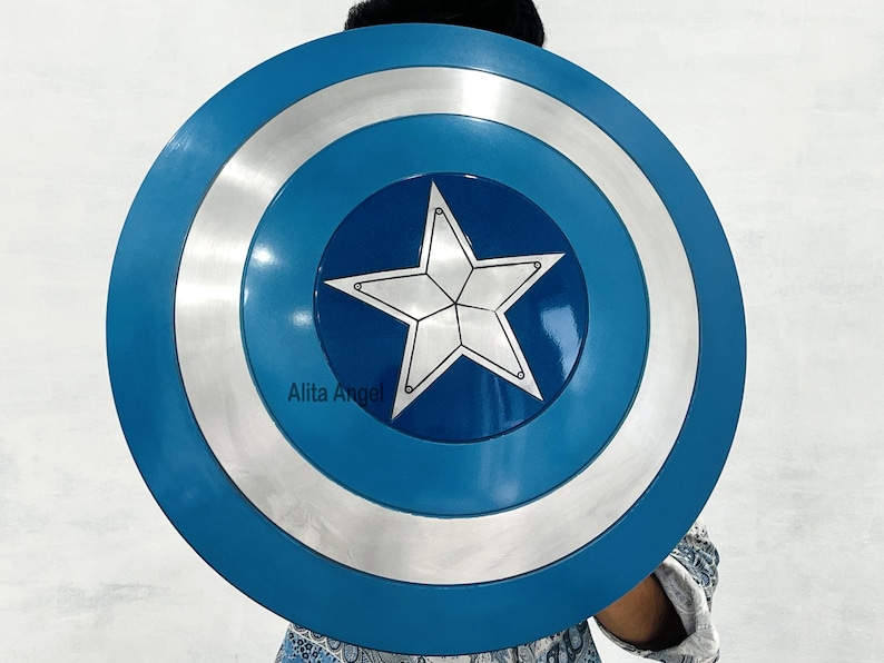 May include: A blue, silver, and white shield with a central white star design. The shield has a circular shape with concentric rings of colour. The shield is a prop or costume accessory.