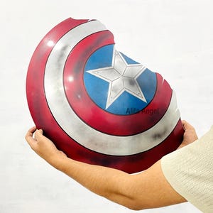 K&ouml;nnte beinhalten: Ein Captain America Schild mit einem Used-Look. Das Schild hat ein rot-wei&szlig;-blaues Farbschema mit einem zentralen blauen Stern auf einem blauen Kreis. Der Schild hat einen Durchmesser von etwa 61 cm.