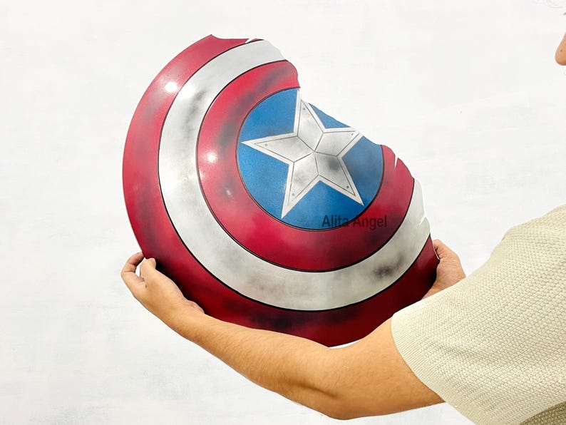K&ouml;nnte beinhalten: Ein Captain America Schild mit einem Used-Look. Das Schild hat ein rot-wei&szlig;-blaues Farbschema mit einem zentralen blauen Stern auf einem blauen Kreis. Der Schild hat einen Durchmesser von etwa 61 cm.