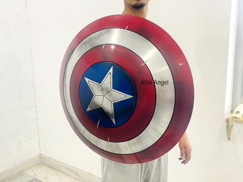 May include: A Captain America shield, featuring a red and white concentric circle design with a blue central area. A white star is centered on the blue area. The shield is round and appears to be made of metal.